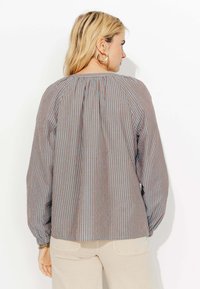 Blouse rayée en bleu et marron, avec un dos froncé, des manches longues et une coupe décontractée. Confectionnée dans un tissu léger au toucher doux.