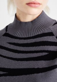 Pull gris à col côtelé, avec des motifs à rayures noires. Texture douce, tricotage serré, adapté pour un style décontracté.