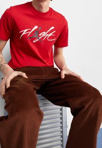 Punainen puuvillapaita, jossa on valkoinen ja harmaa "Flight" -grafiikka siluetilla. Yhdistetty ruskeisiin kammottaviin housuihin, joissa on näkyvä ribbitekstuuri.