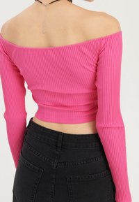 Rosa ribbad off-shoulder topp med långa ärmar, med en kortad design och framhävda midja, tillsammans med en svart högmidjad kjol.