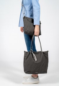 Borsa a spalla grigia con texture liscia e dettaglio a nappina, dotata di manici lunghi; accompagnata da una borsa a tracolla nera più piccola.