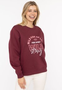 Bordeauxfarbene Sweatshirt mit Rundhalsausschnitt, versehen mit weißen Textmustern: "WILD SIDE OF LIFE FREE SPIRIT WILD STRONG." Weiche Stoffqualität und lockere Passform.