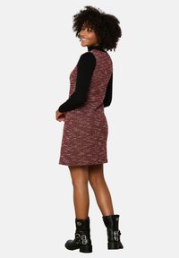 vestido de punto con un patrón texturizado en rojo y negro, mangas largas y una silueta ajustada. Combinado con botas negras hasta el tobillo con hebillas.
