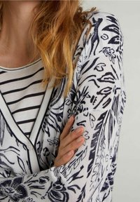 Langärmlige Strickjacke in Weiß mit blauen floralem und abstrakten Mustern, mit Knopfleiste und einem weichen, strukturierten Stoff.