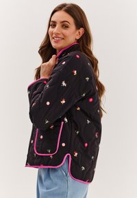 Prešívaná čierna bunda s farebnou výšivkou kvetov a postavičiek, ružovým lemovaním a voľným strihom s bočnými vreckami.