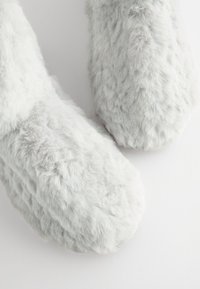 Chaussons gris duveteux avec une surface douce et pelucheuse, un bout arrondi, sans éléments visibles, présentant une légère brillance et un motif texturé.