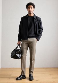 Musta vetoketjullinen takki, musta t-paita, beige-housut, mustat loafersit ja tikattu musta käsilaukku pyöreällä kahvalla.