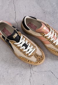 Paire de baskets avec des accents imprimé léopard, panneaux beige et rose, lacets blancs et logo "CAVAL" sur les languettes et les semelles intérieures sur un sol gris fissuré.