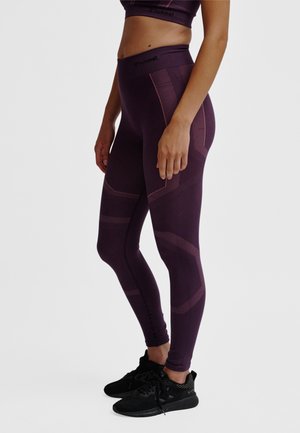 Fioletowe legginsy z teksturowanym wzorem i wysokim paskiem, wykonane z elastycznego materiału. Do tego czarne buty sportowe.