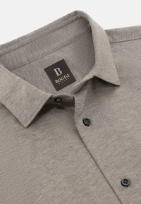 Camicia a strisce beige con colletto a camicia, caratterizzata da un'etichetta nera con logo "B" e bottoni neri su un tessuto testurizzato.