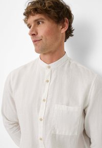 Witte linnen shirt met een bandkraag, sluiting met knopen aan de voorkant en een borstzak. Kenmerkt zich door een zachte textuur en licht, ademend materiaal.