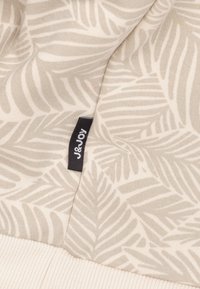 Lichtgekleurde stof met een bladerenpatroon. Inclusief een zwart label met "J&Joy." Gelaagde oppervlakte met geribbelde details aan de onderkant.