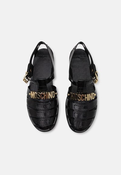 Czarne sandały z lakierowanej skóry ze zapięciem na pasek z tyłu, ozdobione złotymi literami "Moschino" oraz z wyraźną, żłobioną fakturą.