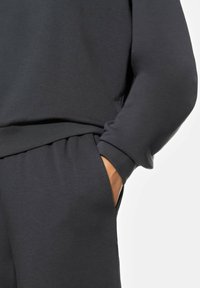 Tummanharmaa collegepaita rentoa istuvuutta, resorihihansuita, sivutaskuja ja sileää pintaa. Kangas vaikuttaa pehmeältä ja mukavalta.