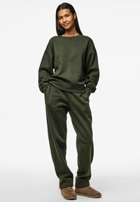 Olivenfarbene Sweatshirt- und Jogginghosenkombination aus weichem Stoff mit lässiger Passform und gerippten Bündchen, kombiniert mit braunen Slippern.