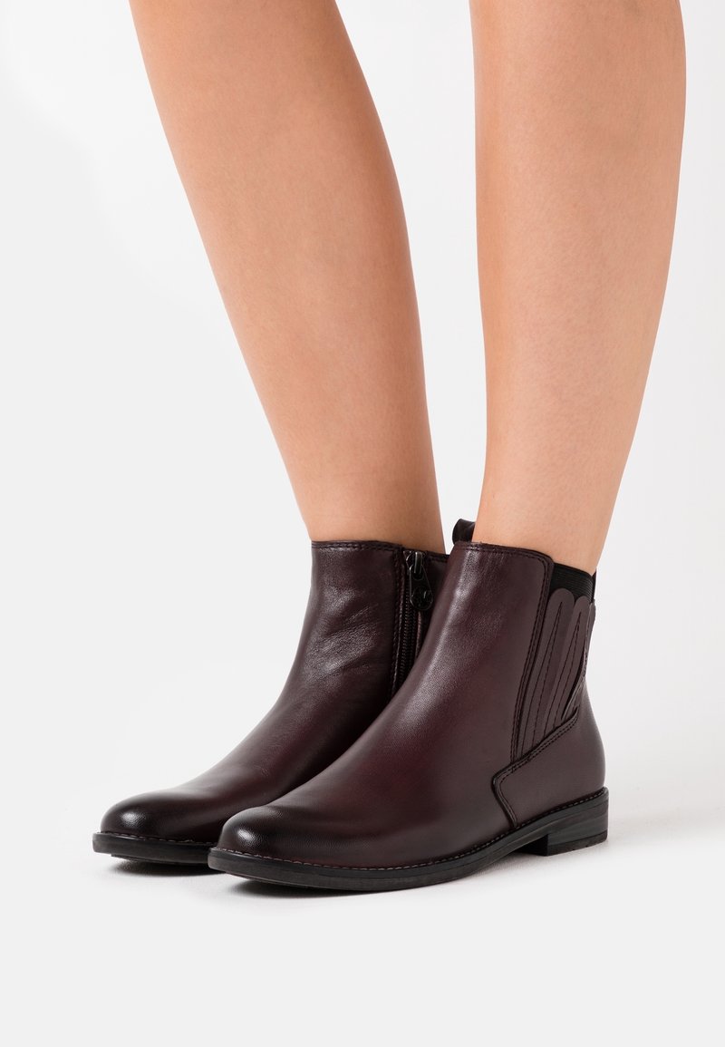 Bottines en cuir bordeaux avec une fermeture éclair latérale, des accents élastiques et un petit talon empilé, présentant une texture lisse et un design à bout rond.