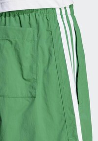 Green shorts with a textured fabric, featuring a side white stripe and a rear pocket. Elastic waistband for adjustable fit.