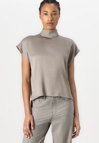 Maglietta grigia chiara a maniche corte con colletto alto, texture liscia e vestibilità rilassata, abbinata a pantaloni grigi coordinati. Design semplice, stile minimalista.