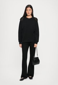 Czarna bluza z teksturowanymi akcentami na ramionach, połączona z czarnymi spodniami dzwonami oraz małą czarną torebką o wzorze krokodyla.