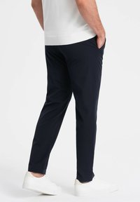 Marineblauwe op maat gemaakte broek van een zachte stof, met een rechte pijp, zijzakken en gedragen met witte sneakers.