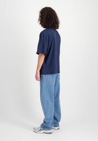 Marineblauw oversized T-shirt met korte mouwen, gecombineerd met lichtblauwe baggy jeans en zilverkleurige sneakers. Zoomdetails zichtbaar op de jeans.