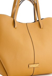 Gelbe Leder-Tote-Bag mit strukturiertem Oberflächenmaterial, doppelten Griffen und einem Magnetverschluss. Mit goldfarbenem Logo-Schild auf der Vorderseite.