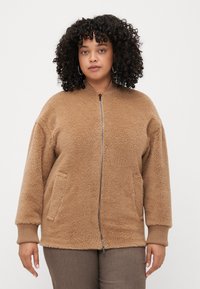 Veste en polaire marron avec fermeture éclair sur le devant, poignets côtelés et deux poches latérales. Texture douce et coupe décontractée, idéale pour un usage quotidien.