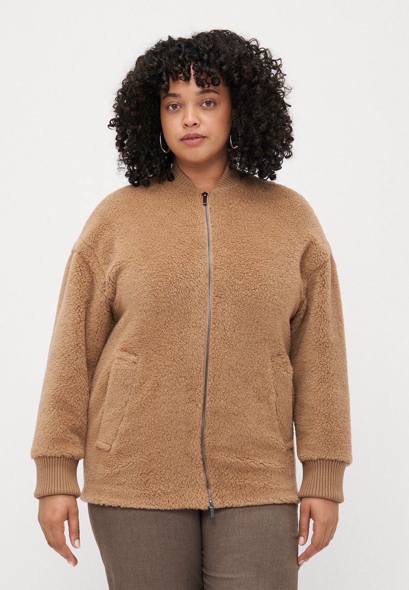 Veste en polaire marron avec fermeture éclair sur le devant, poignets côtelés et deux poches latérales. Texture douce et coupe décontractée, idéale pour un usage quotidien.