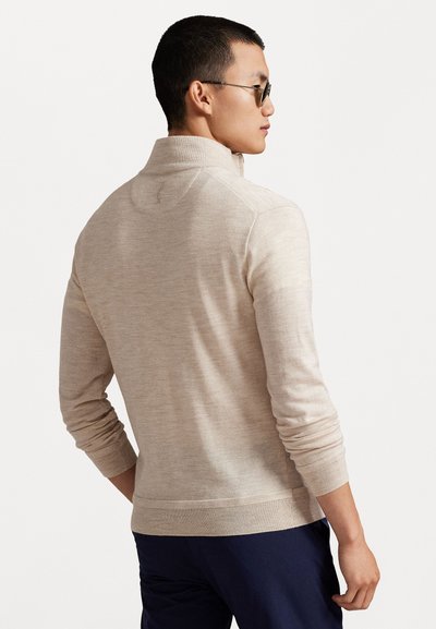 Pull en tricot beige avec un col montant, design ajusté, manches longues, et finitions côtelées aux poignets et à l'ourlet. Pas de motifs visibles ni de détails en métal.