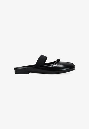 Zapato negro de cuero sin cordones con punta redondeada, banda elástica plana y un nudo decorativo en el frente. Textura suave y diseño minimalista.