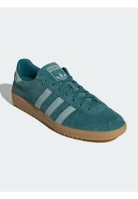 Teal suede athletic shoes with three light blue stripes, a rubber sole, and a padded collar. Features a logo on the tongue.