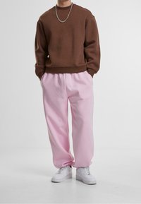 Felpa marrone a girocollo, pantaloni della tuta rosa a vestibilità ampia e sneakers bianche. Il tessuto sembra morbido; la felpa ha polsini e vita a coste.