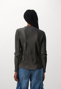Maglietta a maniche lunghe, in grigio scuro con texture liscia. Presenta un collo rotondo e cuciture a contrasto, abbinata a pantaloni cargo blu.