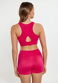 Fuksia urheiluliivit, joissa on urheilullinen racerback-muotoilu ja avainaukolla, yhdistettynä vastaaviin korkeavyötäröisiin shortseihin. Sujuva, joustava kangas.