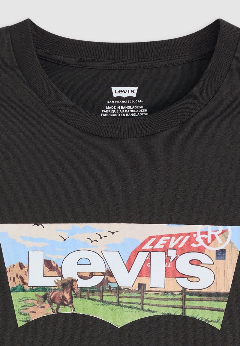 Czarna bawełniana koszulka z nadrukiem vintage logo Levi's, przedstawiająca krajobraz z koniem, stodołą, trawą i ptakami, otoczona kolorową grafiką.