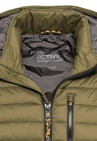 Olivgrüne Pufferjacke mit einem Reißverschluss vorne. Das Innenfutter ist grau und trägt das Branding "Camel Active Recycled". Enthält verstellbare Kordelzüge.