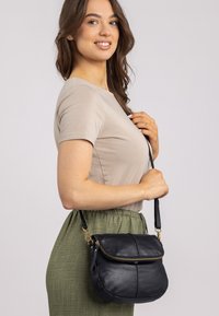 Schwarze Leder-Umhängetasche mit Reißverschluss, runder Form und goldenen Hardware-Details. Texturierte Oberfläche mit dezenten Nähdetails.