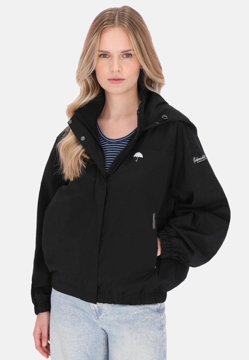 Zwarte waterdichte jas met een opstaande kraag, elastische manchetten en een wit logo op de borst. Zachte stof met een ontspannen pasvorm.