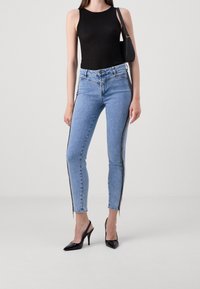 Jeans azul claro de corte ajustado con detalle de cremallera lateral, combinados con una camiseta sin mangas negra de canalé y tacones negros de punta.