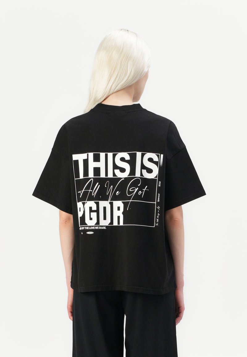 T-shirt nera oversize con testo bianco in grassetto sul retro: "QUESTO È TUTTO QUELLO CHE ABBIAMO PGDR" con un ulteriore elemento grafico.