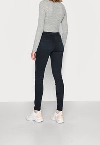 Jeans ajustados y de tiro alto en denim oscuro, con dos bolsillos traseros y una textura suave. Combinados con zapatillas blancas y beige.