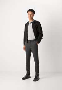 Veste noire avec fermeture à boutons-pression, t-shirt gris, pantalon slim gris, et chaussures noires à lacets. Textures lisses et design minimaliste.