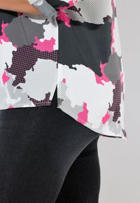 Losse blouse met een abstract patroon in roze, grijs en wit; materiaal lijkt lichtgewicht en soepel; randen zijn afgerond.