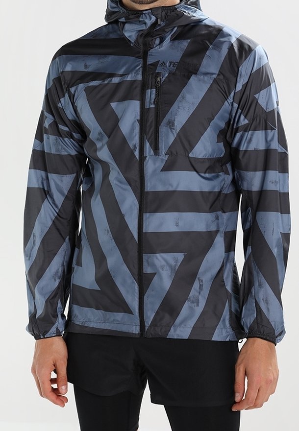 Veste légère à capuche de couleur noire avec des motifs géométriques bleus. Comprend une poche poitrine zippée et des poignets élastiques pour un ajustement sécurisé.