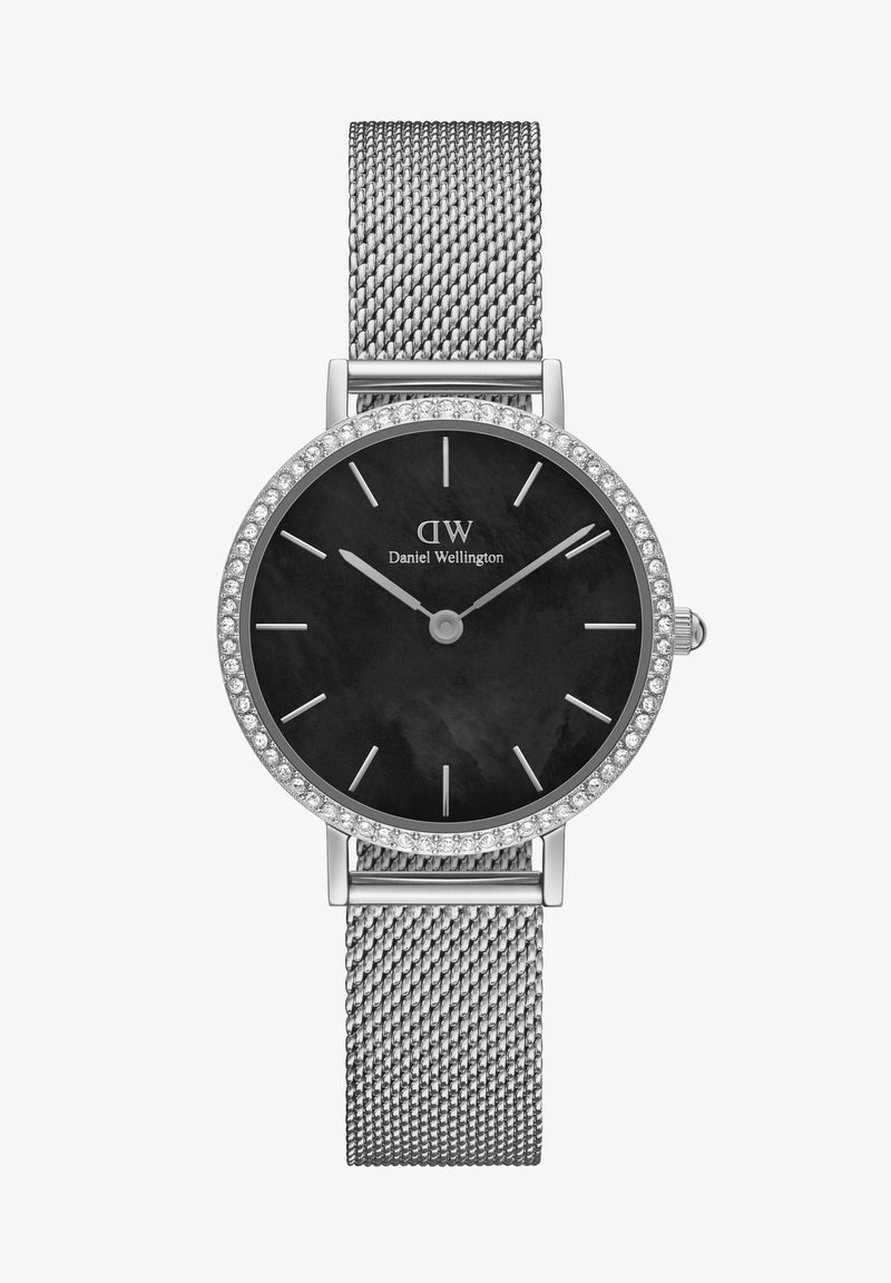 Hõbedane võrksiidiga kell, millel on ümmargune must kellakuul, mida kaunistavad sädelev kristallist kellakeer ja minimalistlikud hõbedased tundemarkid, samuti brändi logo.