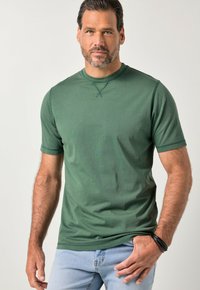 Green short-sleeve t-shirt made of smooth fabric. Round neckline with cross-stitch detailing, paired with light blue jeans.
