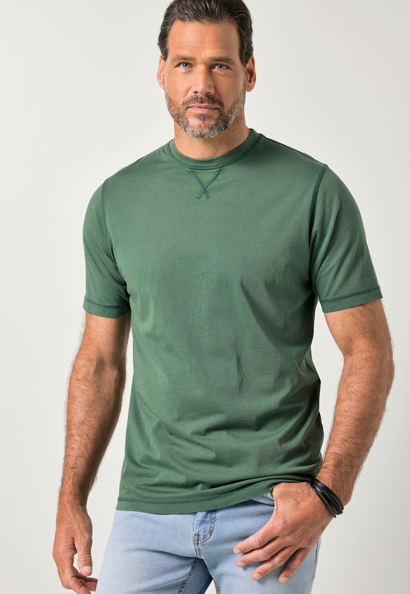 Green short-sleeve t-shirt made of smooth fabric. Round neckline with cross-stitch detailing, paired with light blue jeans.