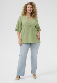 Light green textured top with a V-neck and elbow-length sleeves, paired with light blue straight-leg jeans and nude high-heeled shoes.