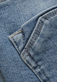 Blauwe denim stof met een driehoekige flapzak. De textuur is iets ruw en heeft contrasterende beige stiksels langs de randen.