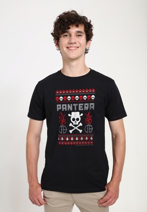 Ung mand smiler og bærer en sort T-shirt med rød, hvid og grå kranie- og flammegrafik samt teksten "PANTERA" på forsiden.
